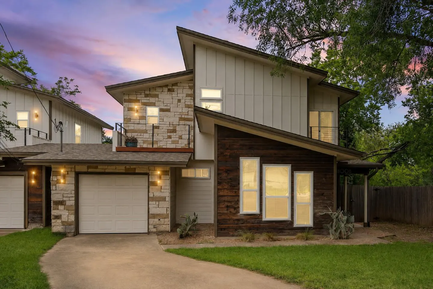 Modern two-story house with stone, wood, and white siding, a white garage door, and a sloped roof against a twilight sky.