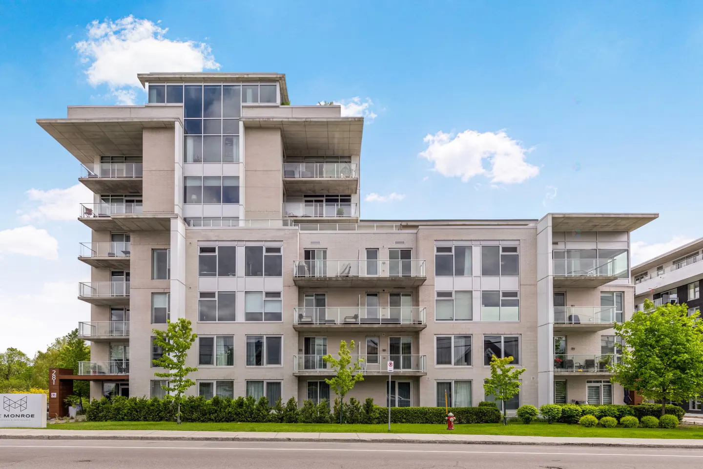 Exterior view of a modern, multi-story apartment building with balconies and large windows under a blue sky.