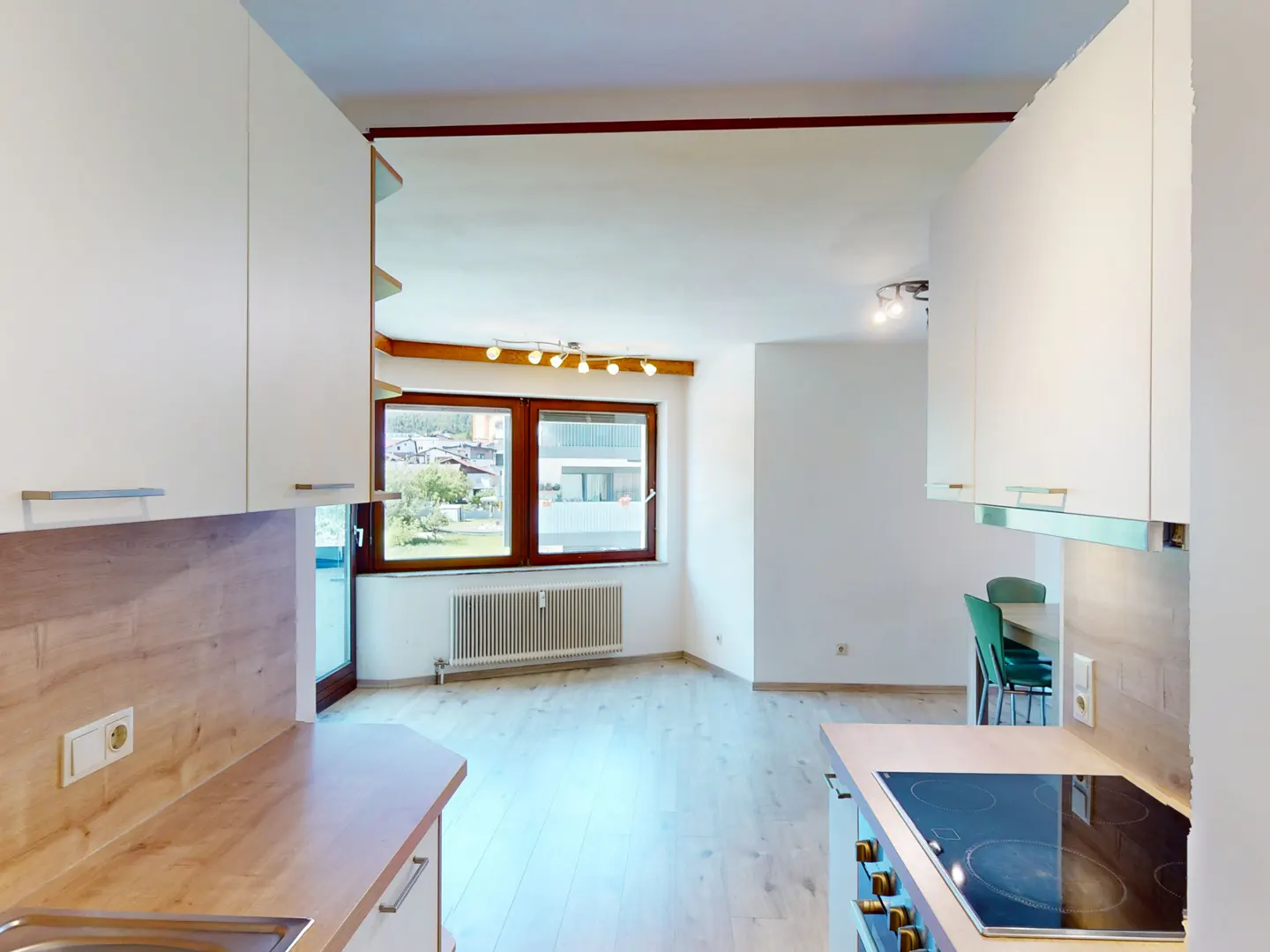A bright, modern kitchen with white cabinets, wood countertops, and a window overlooking a town. A stove and dining table are visible.