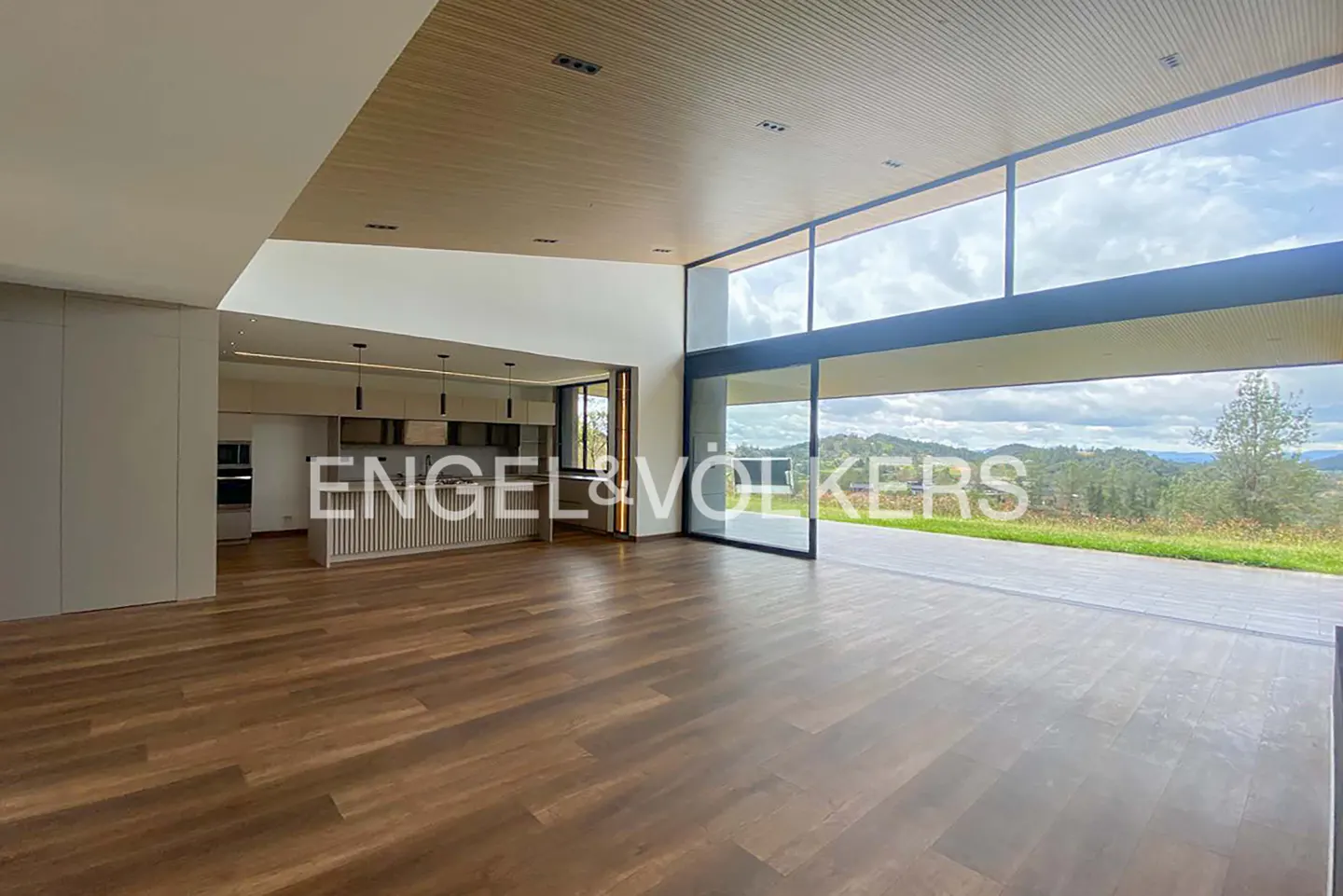 Modern open-plan living area with wood floors, a sleek kitchen, and floor-to-ceiling windows overlooking a scenic landscape.