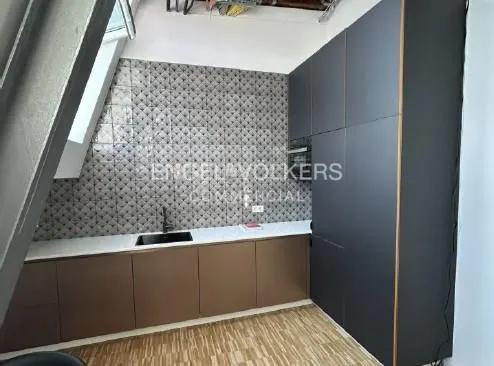 Modern kitchen with gray cabinets, brown lower cabinets, white countertop, and patterned gray backsplash. Wood floor and skylight.