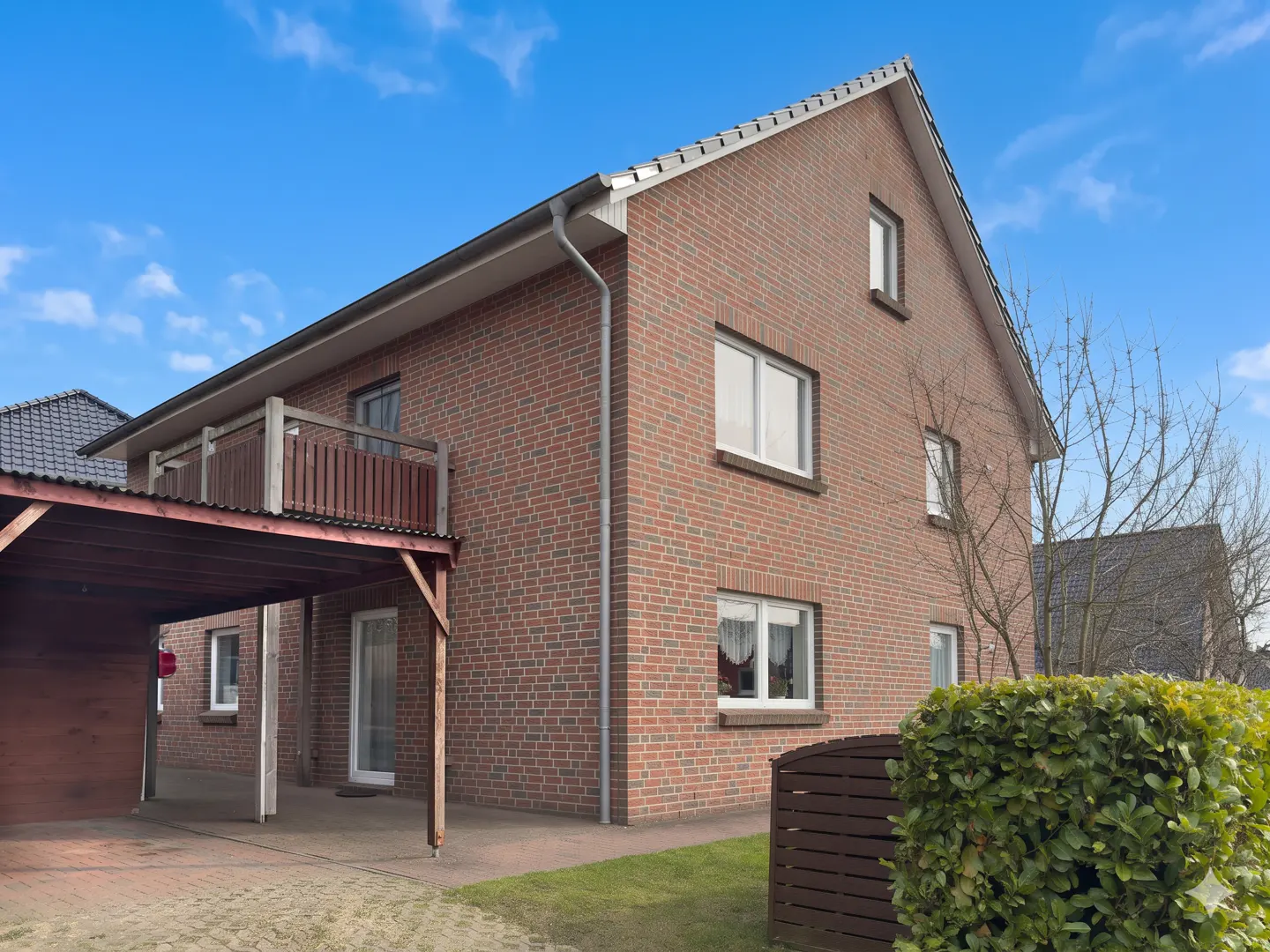 Two-story brick house with white-framed windows, a balcony, and a carport under a blue sky.