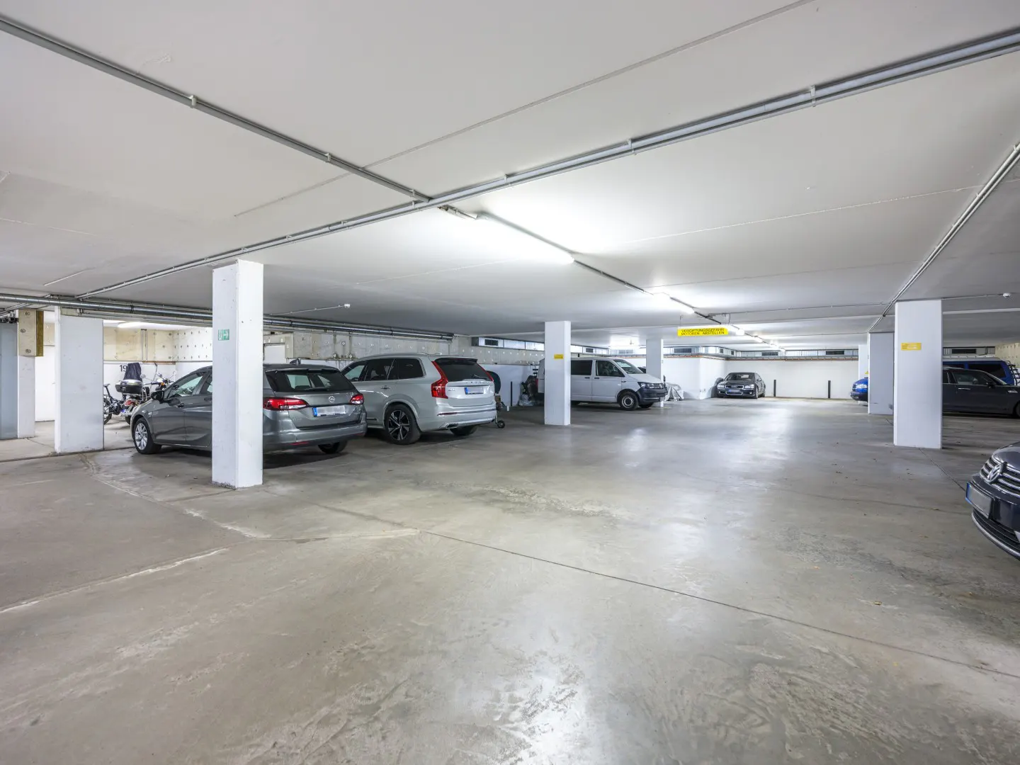 Brightly lit parking garage with several parked cars and white support columns.