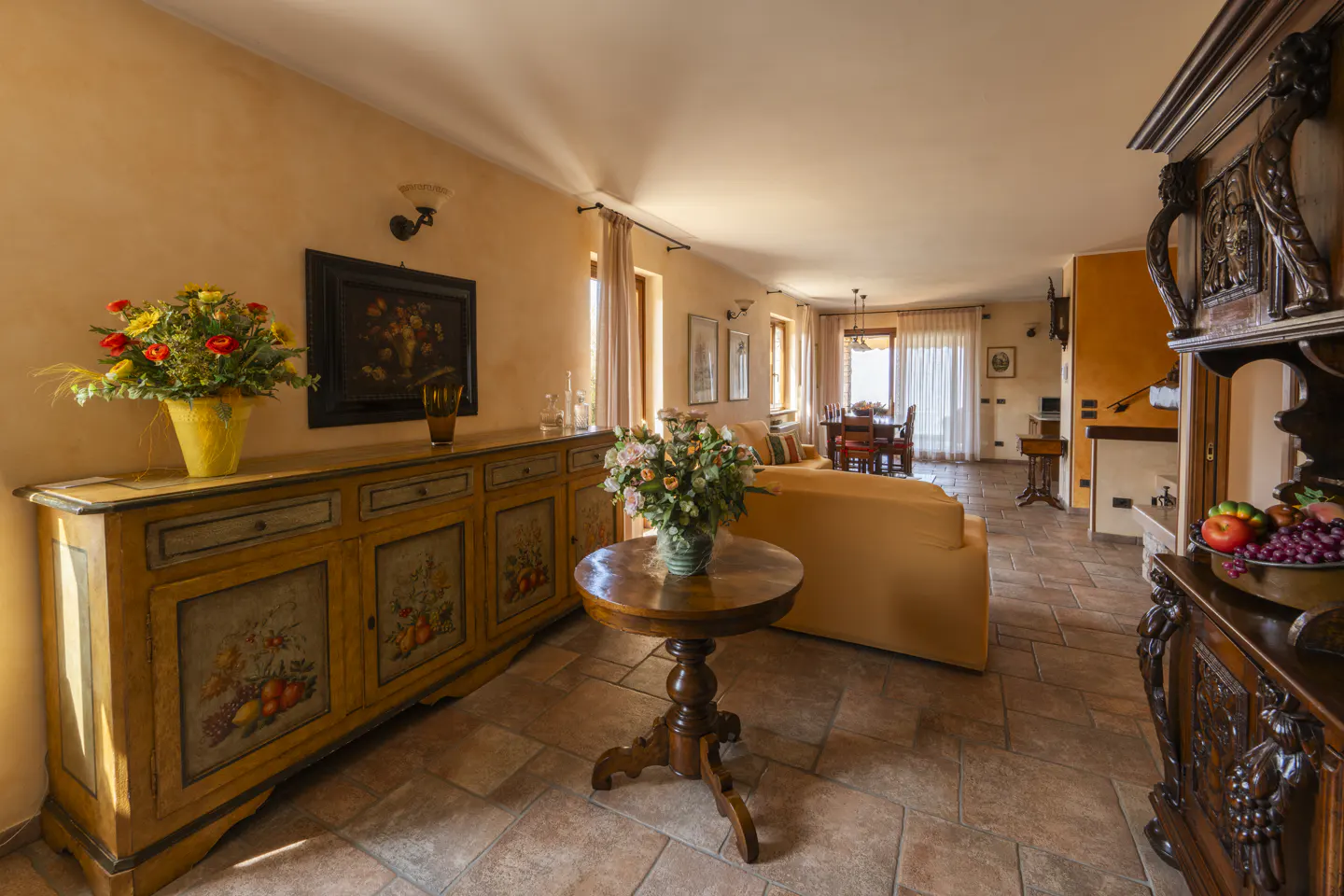 A warm living room with terracotta tile floors, antique furniture, and a dining area in the background.