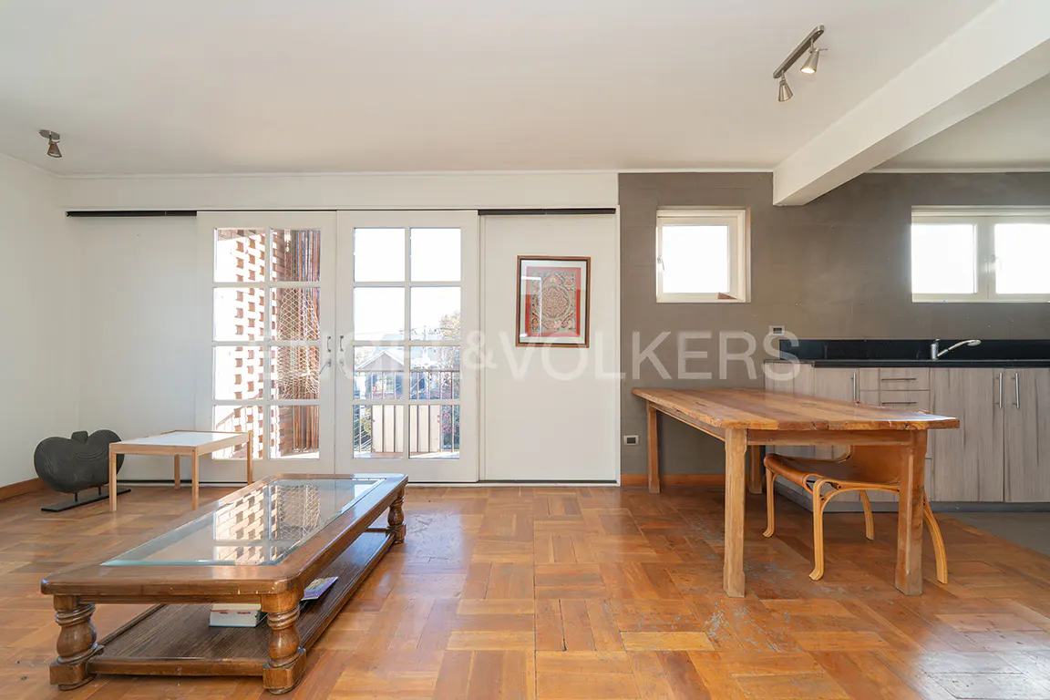 Bright living room with parquet floors, a glass-topped coffee table, and a wooden dining table near a kitchen area. White sliding doors lead to a balcony.