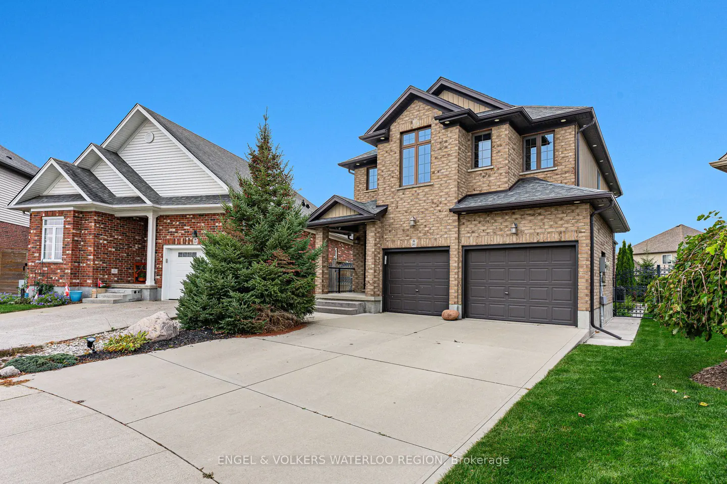 Two-story brick house with a two-car garage and a long concrete driveway on a sunny day.