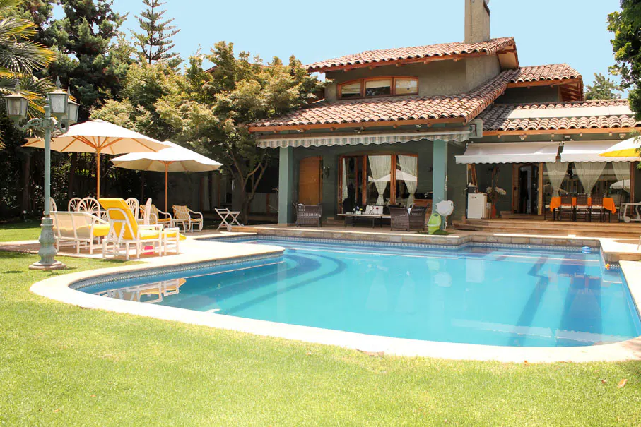 A backyard with a blue swimming pool, green grass, and a two-story house with a red tile roof.