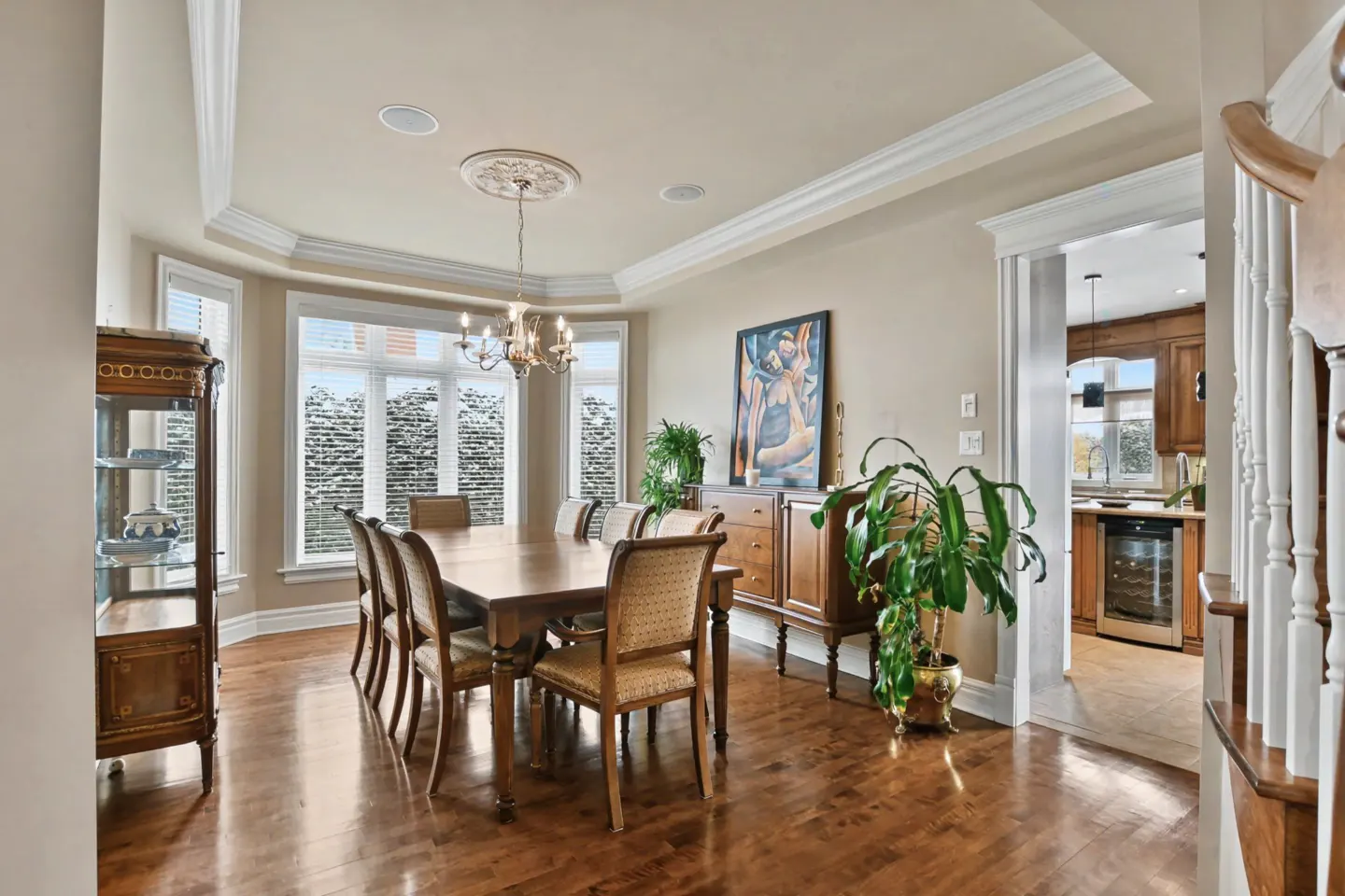 A dining room with a wood table, chairs, and hardwood floors. A china cabinet and buffet are against the walls. A chandelier hangs from the ceiling.
