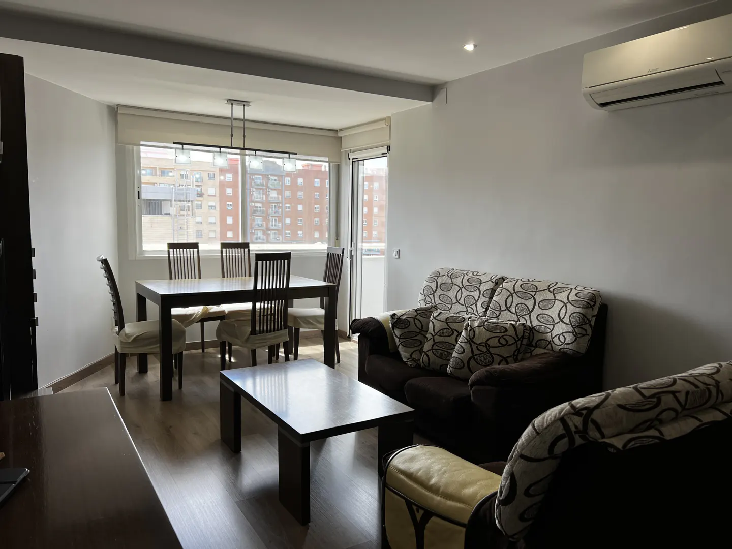 A bright living room with a dining table, a brown sofa, and a coffee table.