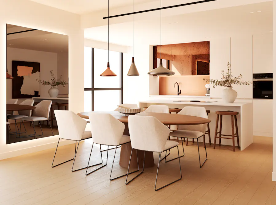 Bright, modern dining area with a round wooden table, white chairs, and pendant lights. A large mirror reflects the kitchen with white cabinets and copper accents.