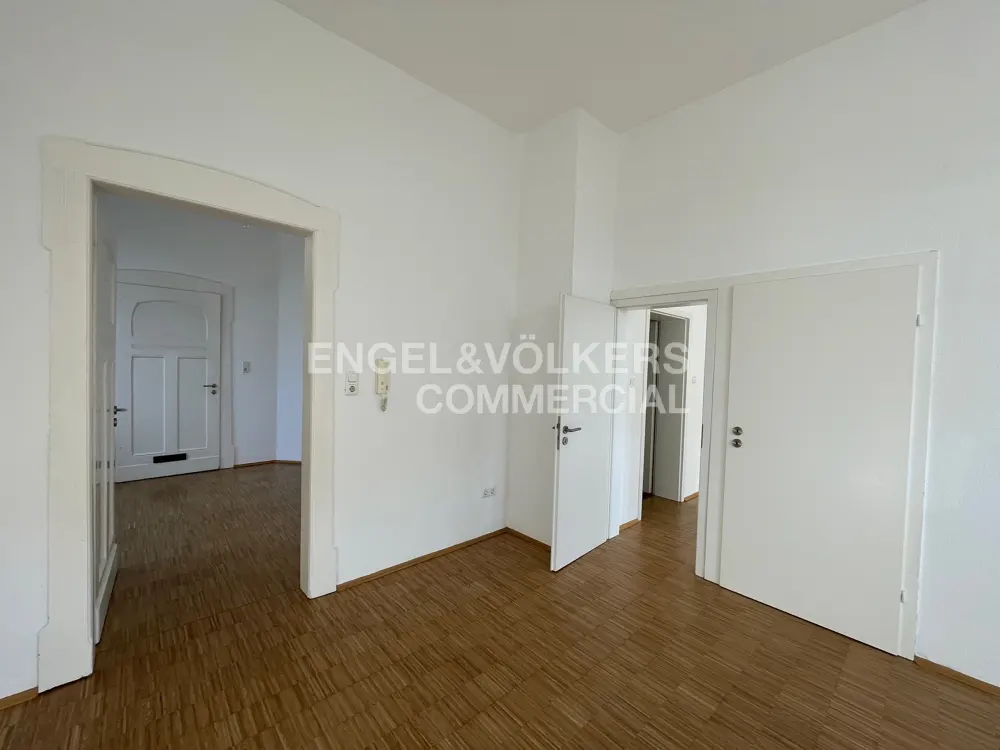 Bright room with wood floors, white walls, and doors. Engel & Völkers Commercial logo on the wall.