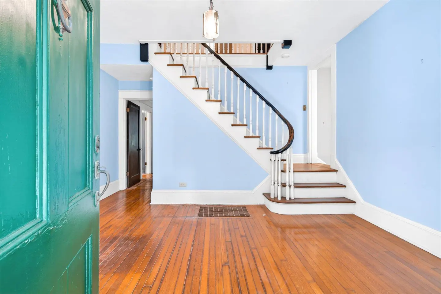 Open green front door reveals a foyer with hardwood floors, blue walls, and a staircase with white railings.