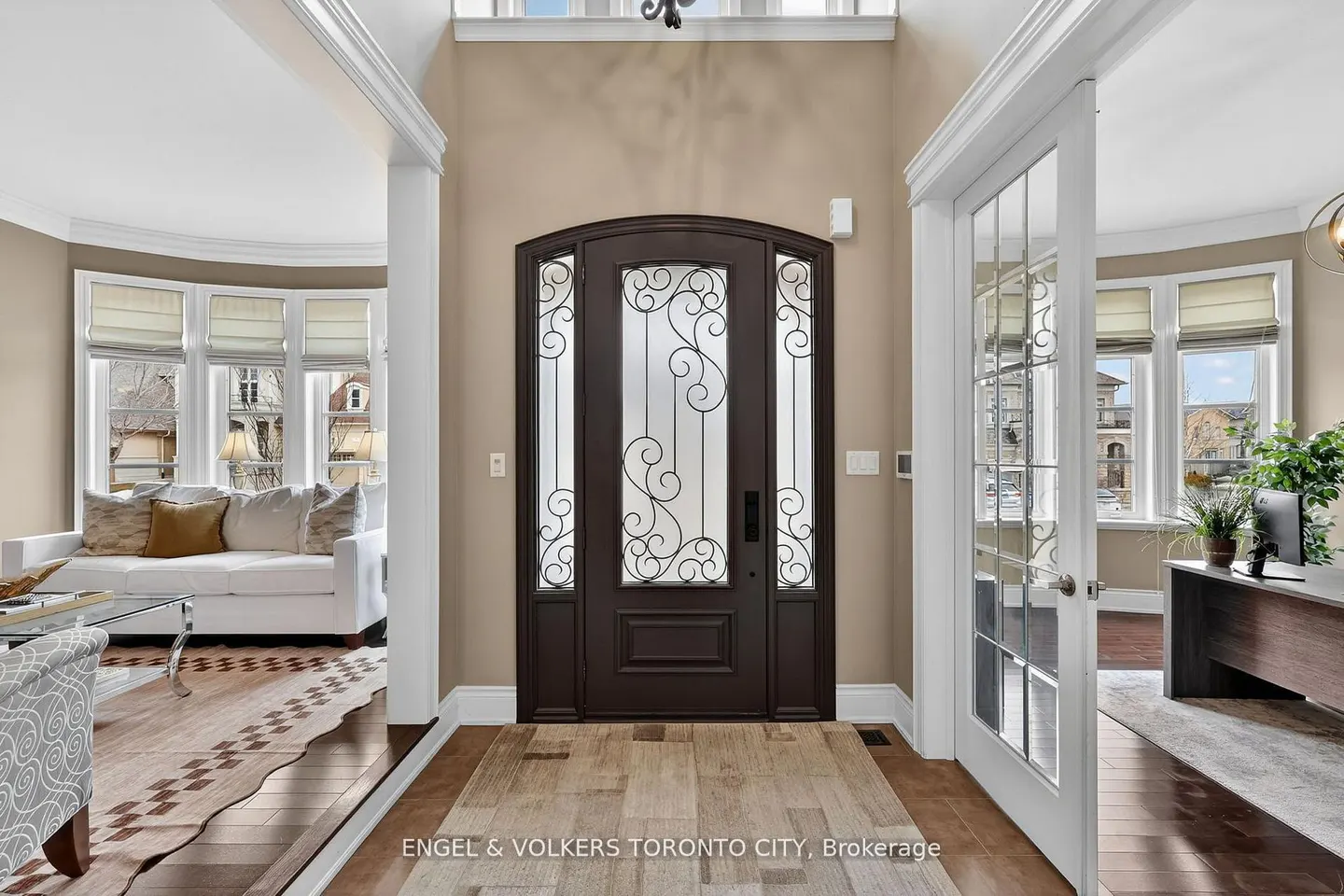 Grand foyer with a dark arched door featuring iron scrollwork, flanked by a living room and a home office with glass doors.