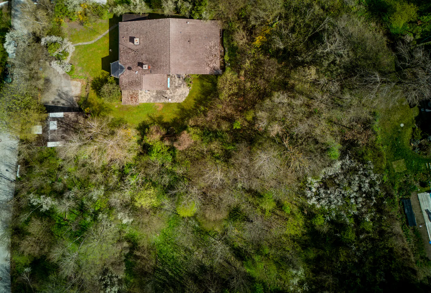Aerial view of a house with a brown tile roof surrounded by green trees and grass.