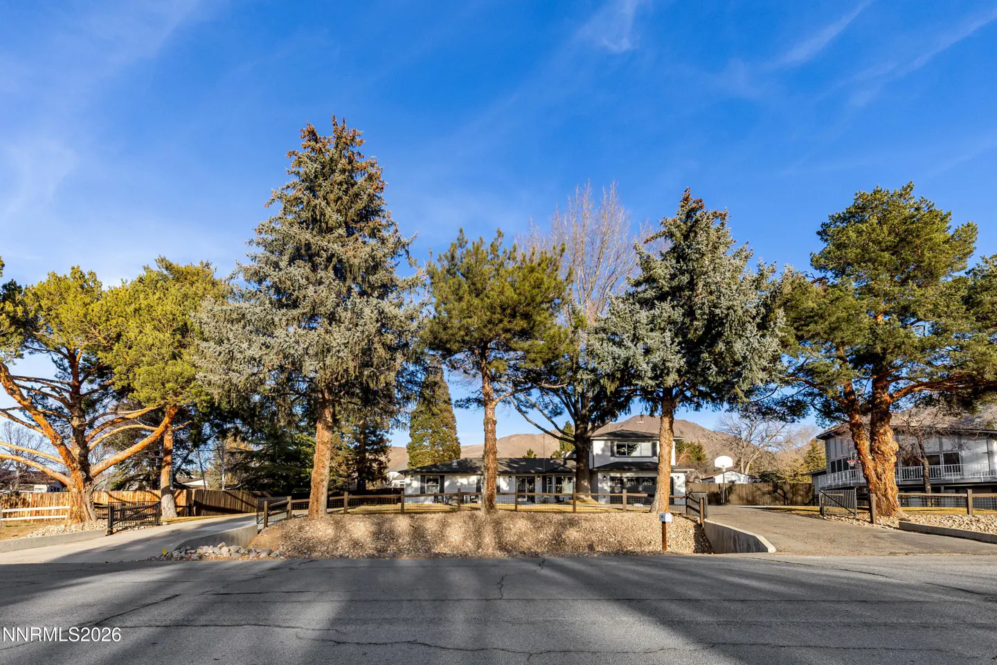 A single-family home with a gray exterior is surrounded by tall trees under a bright blue sky.