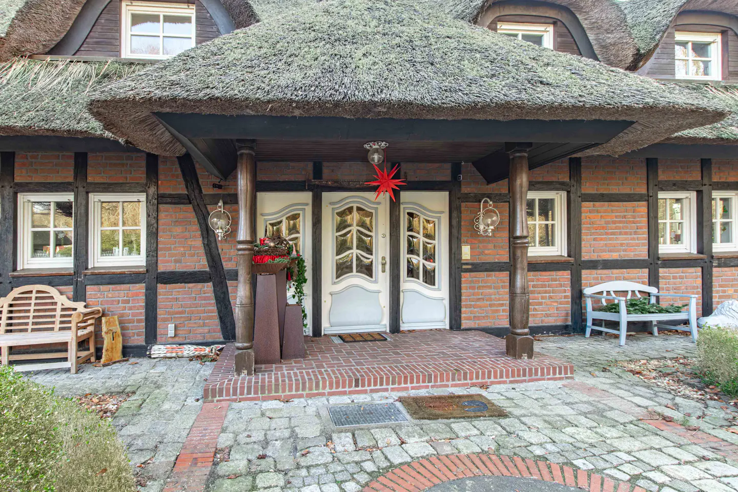 Exterior of a brick house with a thatched roof and a white double door entrance. A red star hangs above the door.