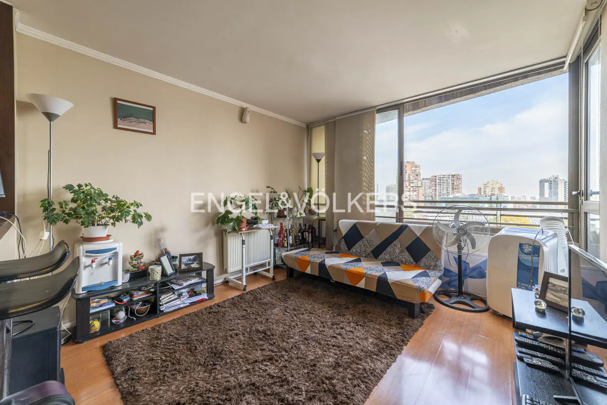 Living room with a brown shag rug, patterned sofa, floor fan, and large windows overlooking a city skyline.