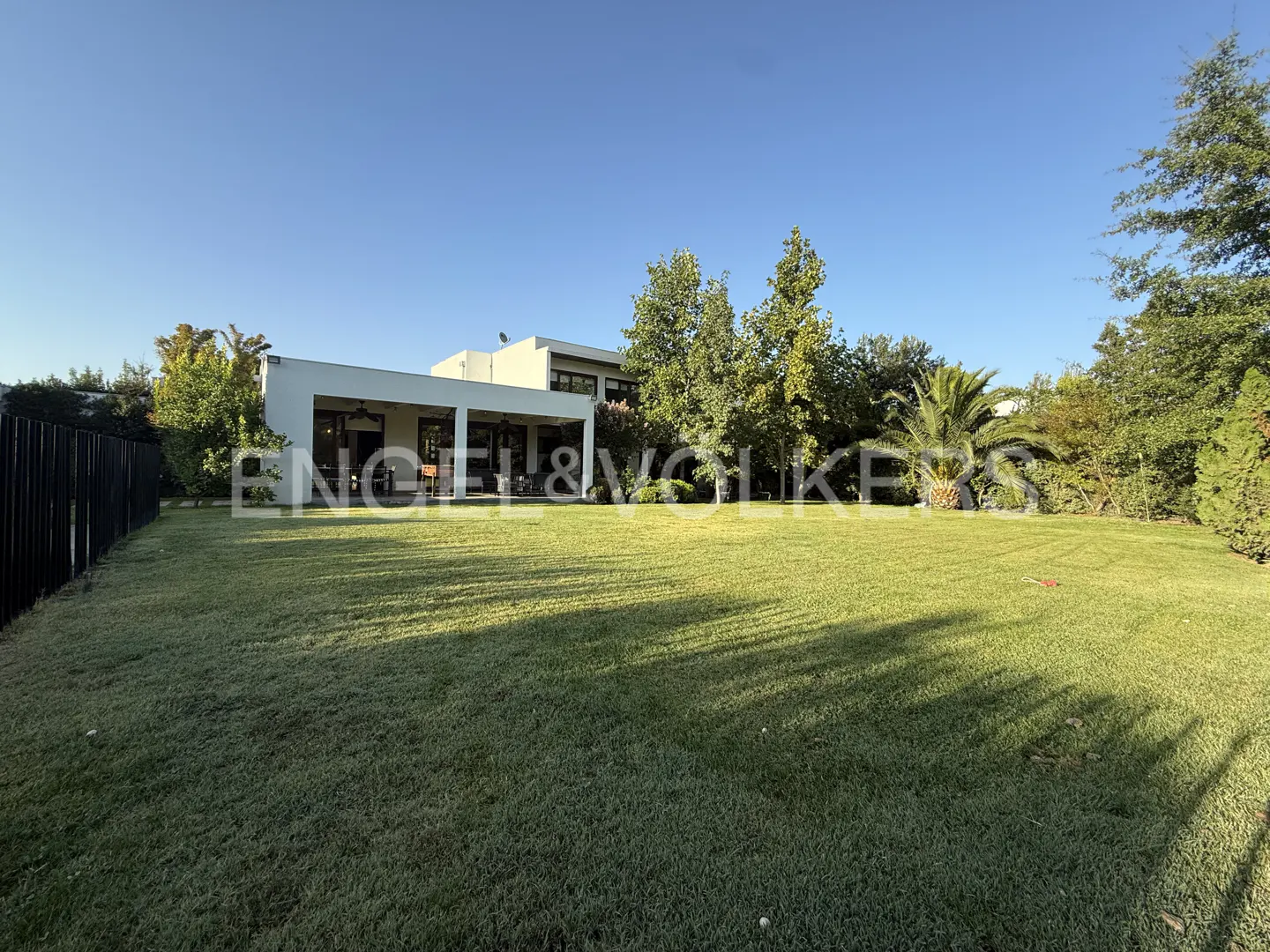 Wide shot of a modern white house with a large green lawn and trees under a blue sky.