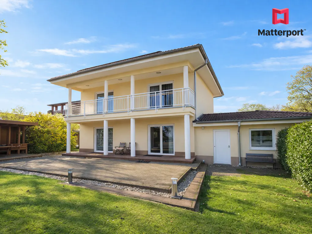 Two-story yellow house with white balcony and pillars, patio, green lawn, and blue sky.