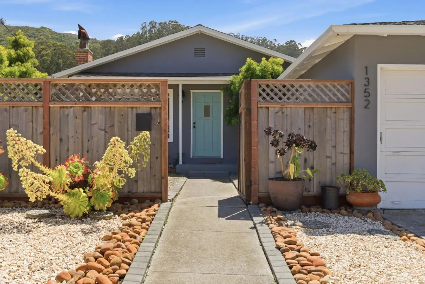 Exterior of a gray house with a light blue door, wood fence, and stone walkway.