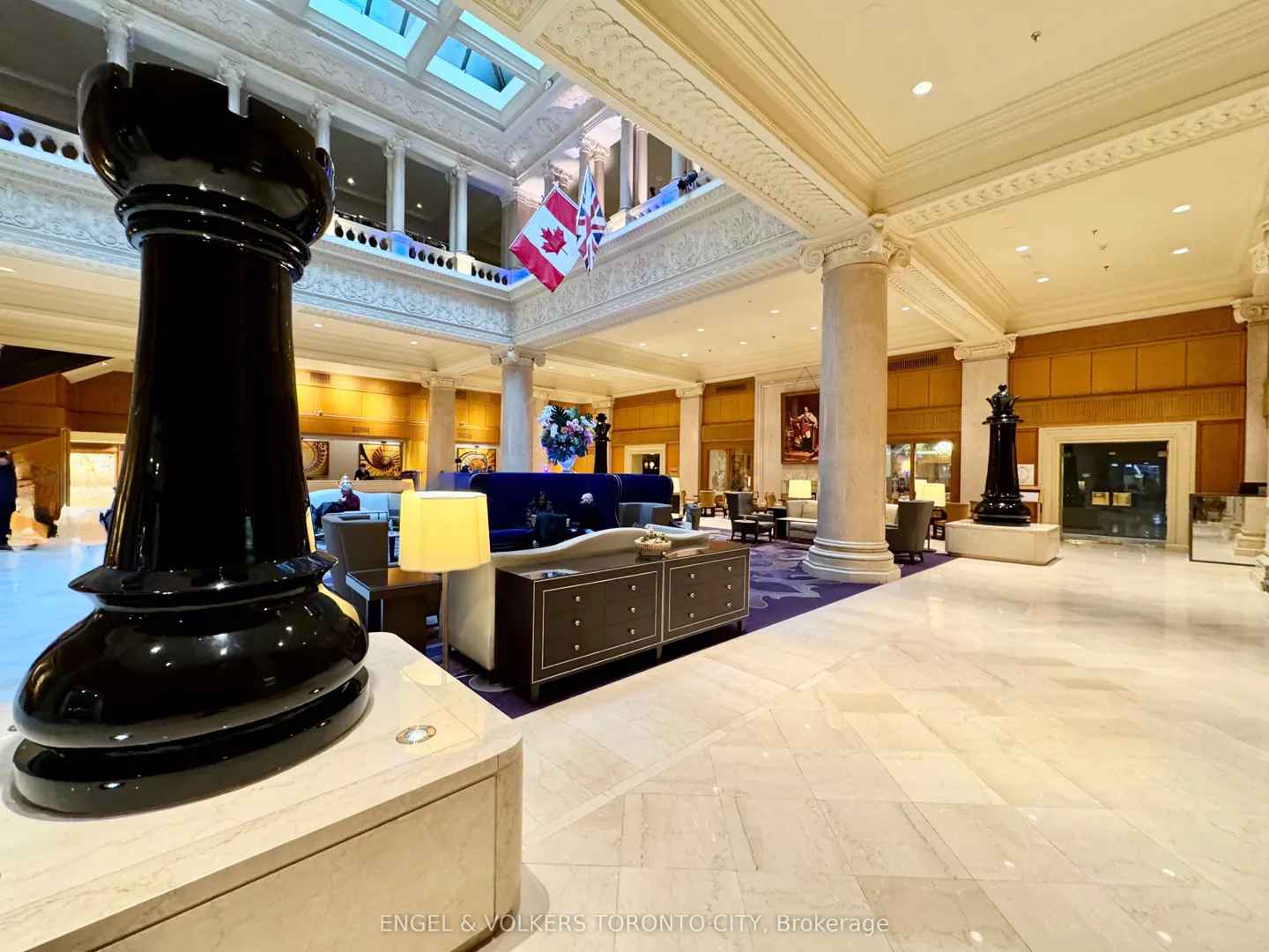Hotel lobby with marble floors, columns, and a large black chess piece. Flags hang from the upper level. Seating areas are visible.