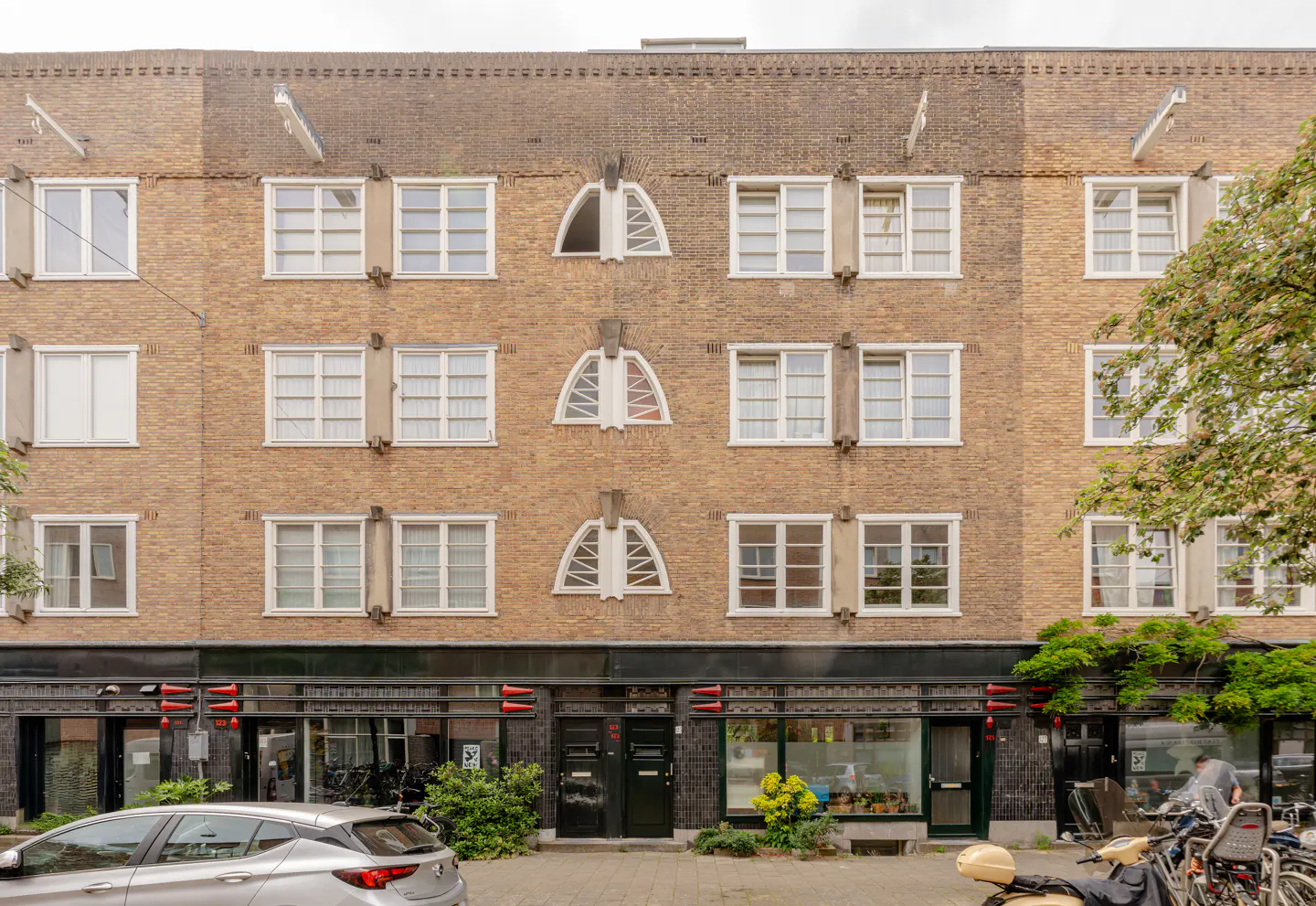 Exterior view of a multi-story brown brick apartment building with white-framed windows and arched architectural details.