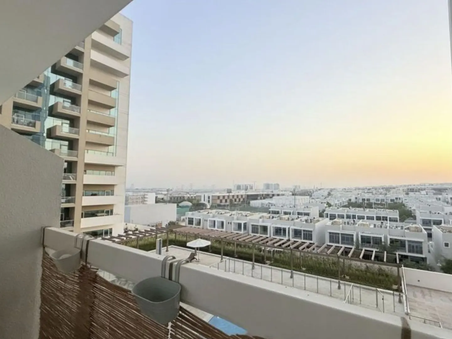 View from a balcony overlooking a residential area with white houses and a tall building under a light blue sky.