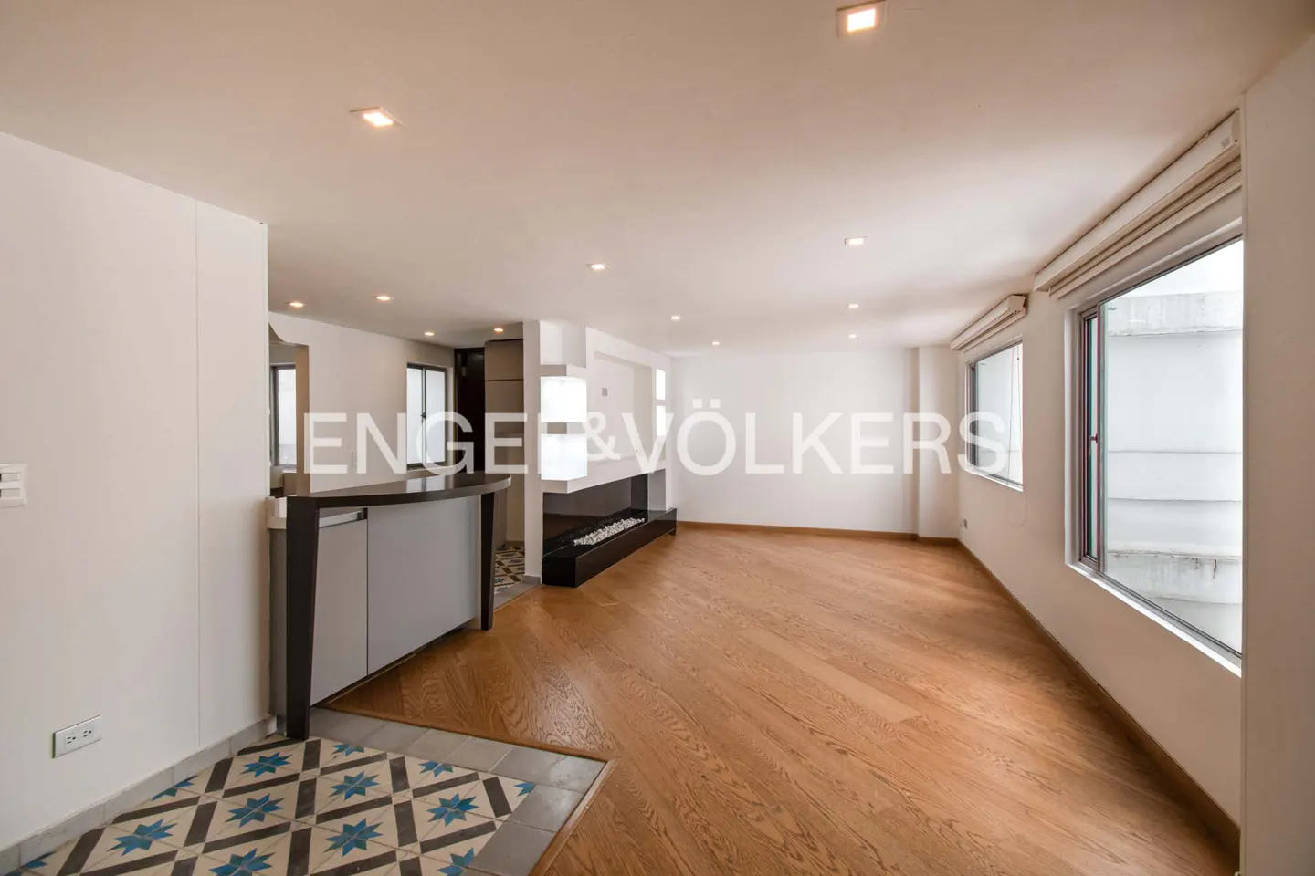 Bright, open living space with hardwood floors, a modern fireplace, and large windows. A bar area with patterned tile adds character.
