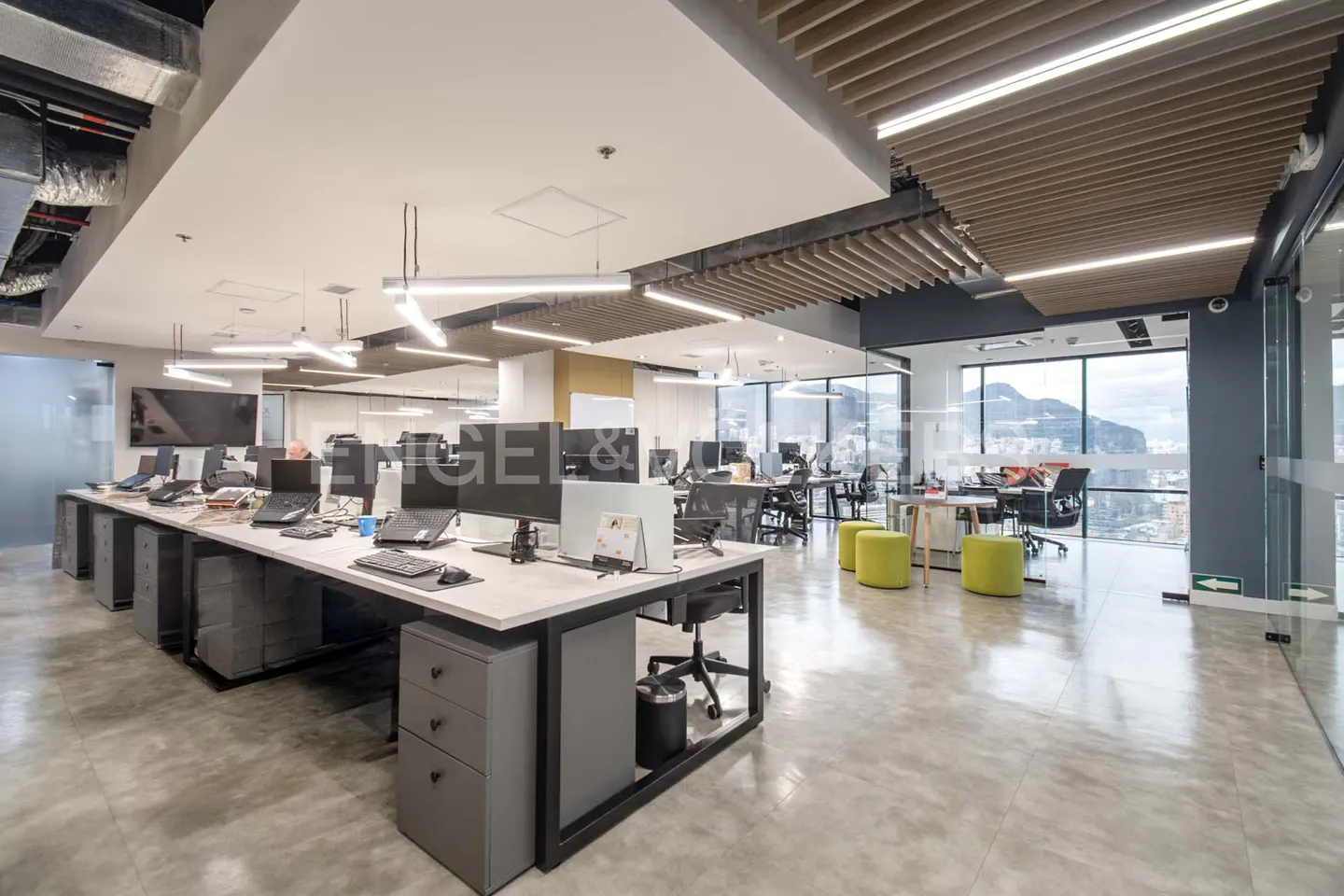 Bright, modern office space with desks, computers, and large windows overlooking a city and mountains.