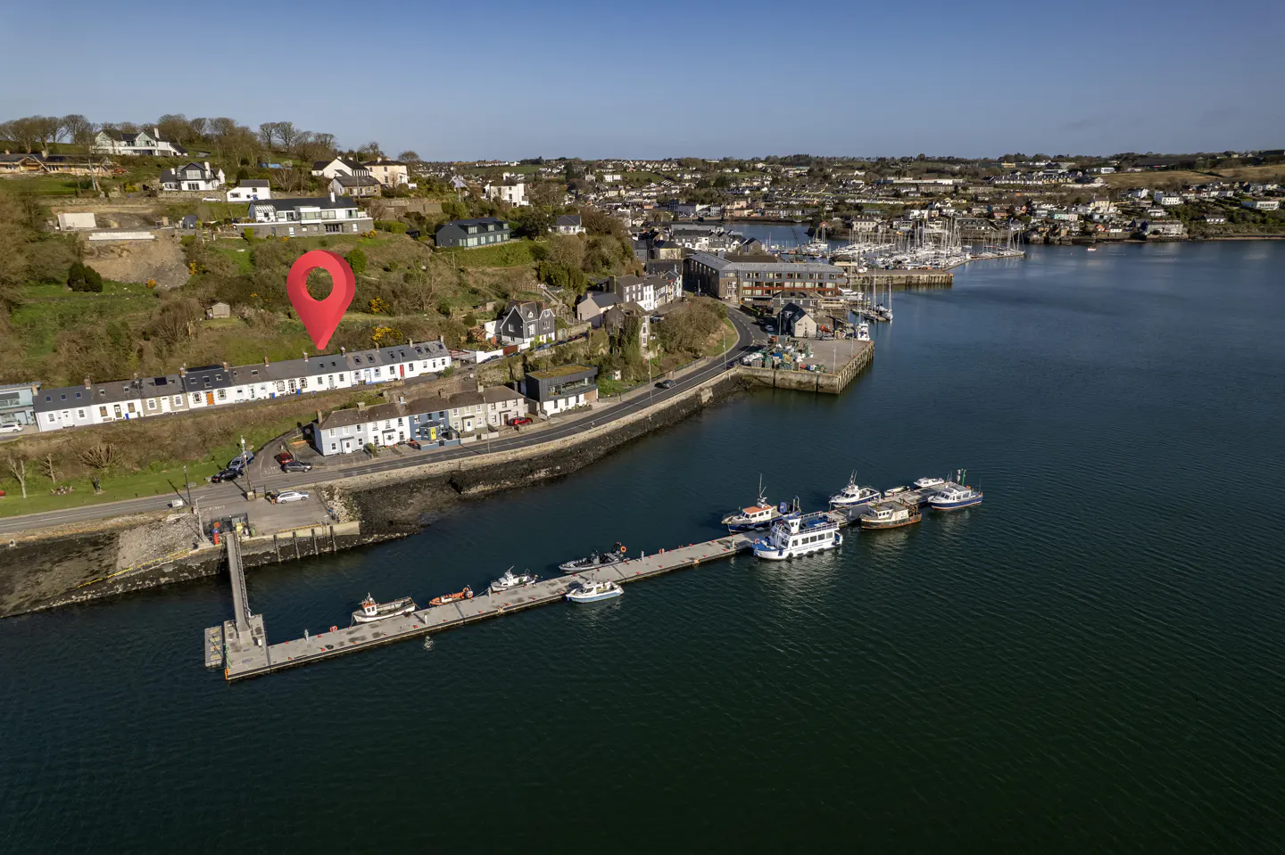 Aerial view of waterfront property with a red location pin, pier, boats, and harbor.