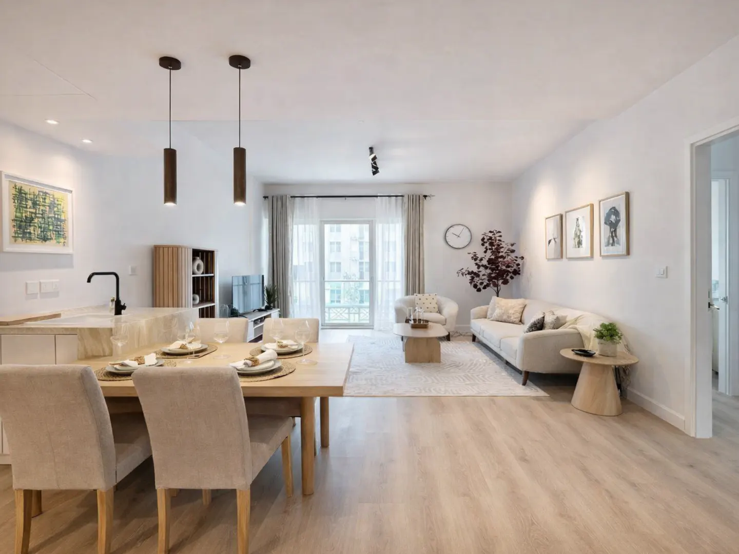 Modern open-plan living area with a dining table, beige sofa, light wood floors, and a balcony with natural light.