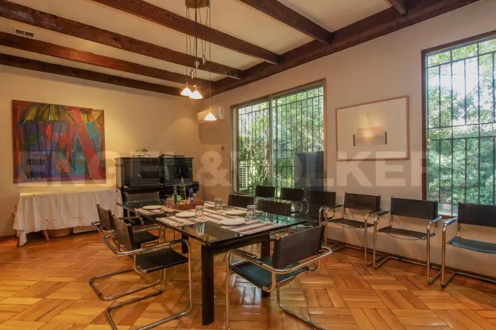 A dining room with a glass table, black chairs, wood floors, and a piano in the background.