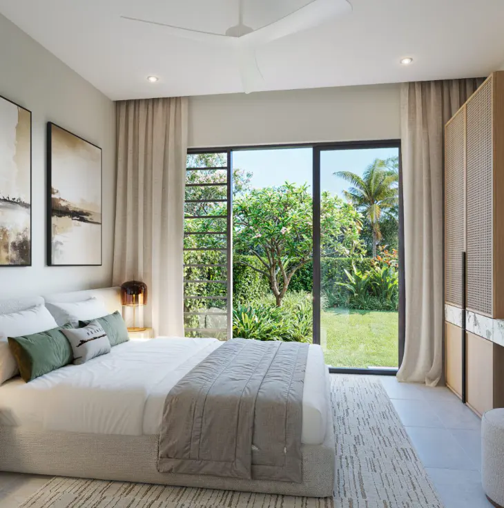 Bright bedroom with a white bed, green pillows, and a gray blanket. Large windows overlook a lush green garden. A white ceiling fan is visible.