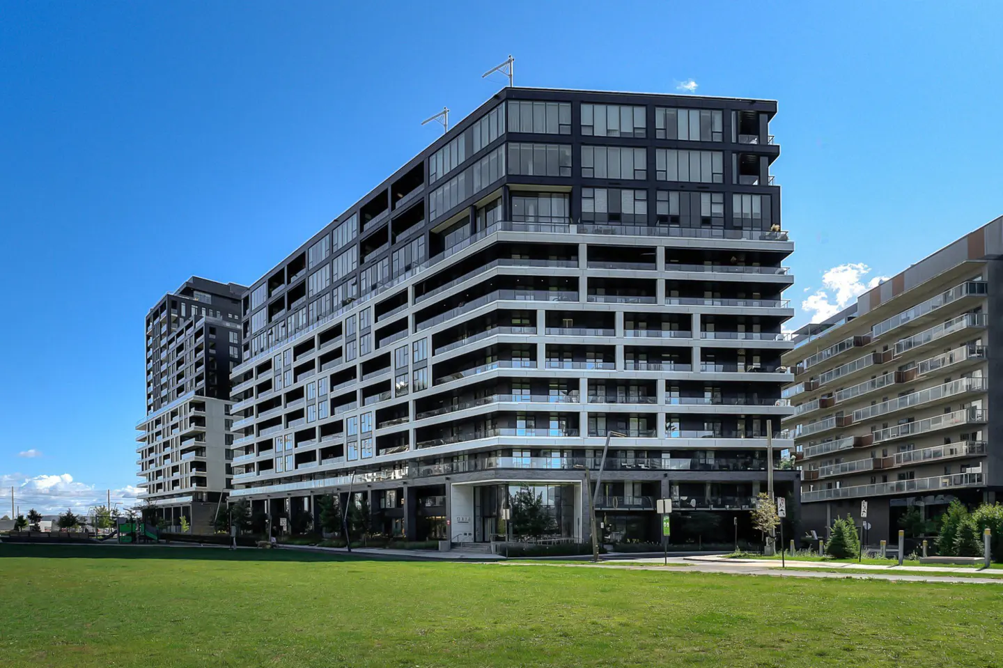 Modern condo building with black and white balconies, set against a bright blue sky and green lawn.