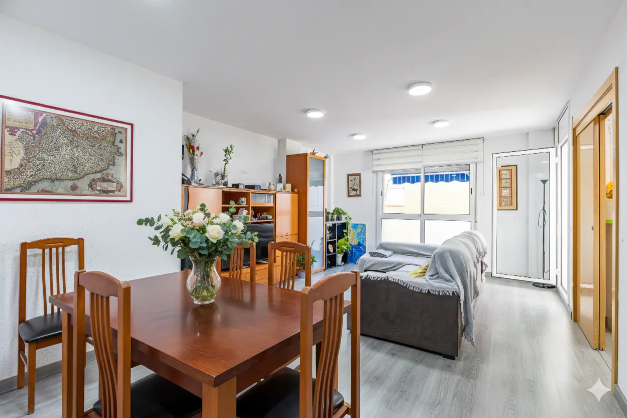 Bright living and dining area with a wooden table, chairs, and a gray sofa with a blanket. A map hangs on the wall.