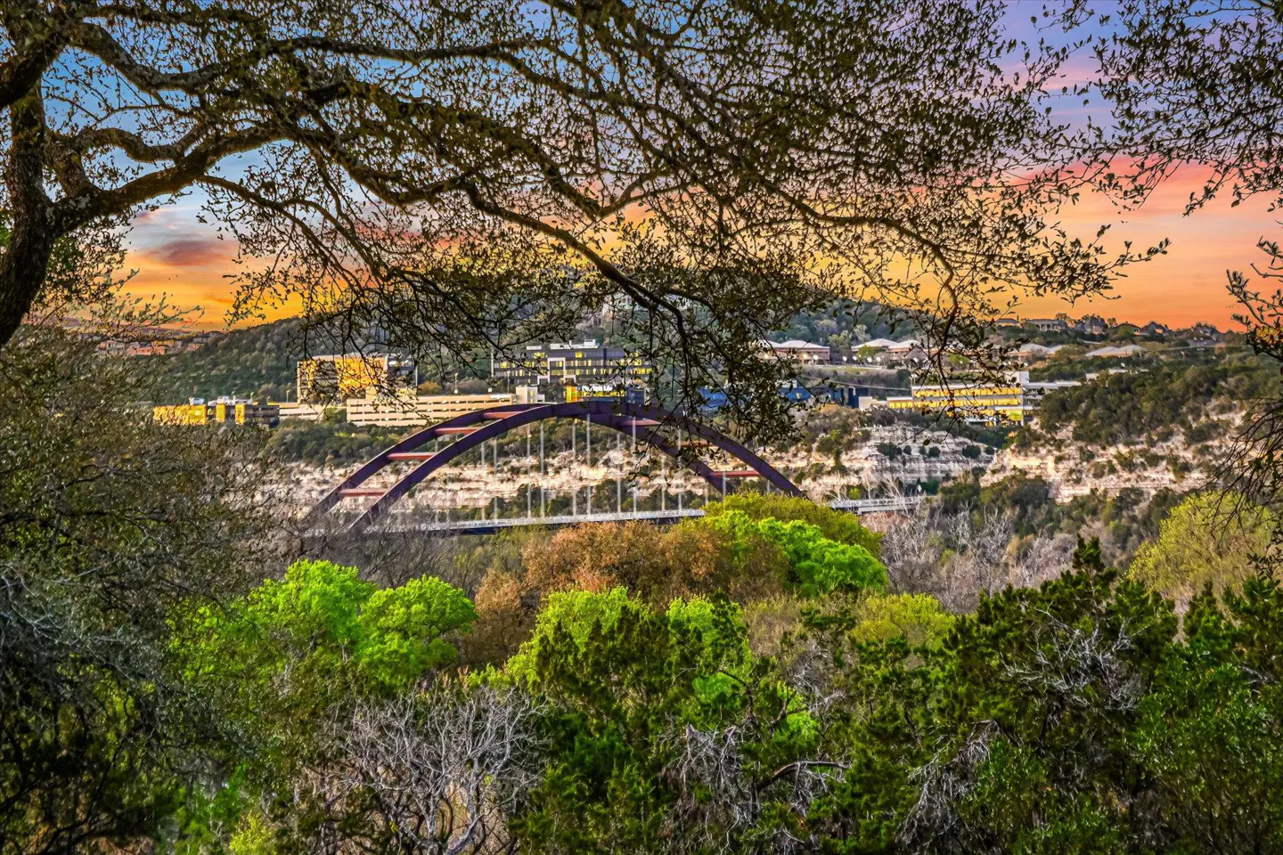 View of the Pennybacker Bridge in Austin, Texas, framed by trees at sunset.