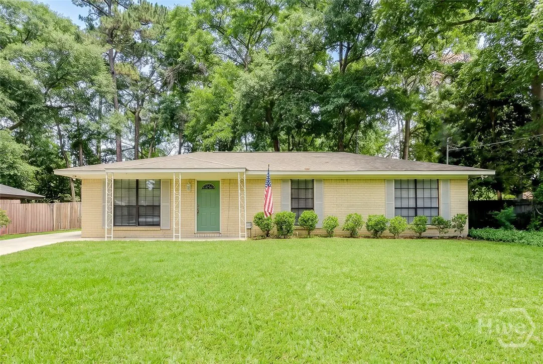 A ranch-style house with a green door, yellow brick, and an American flag on a green lawn.
