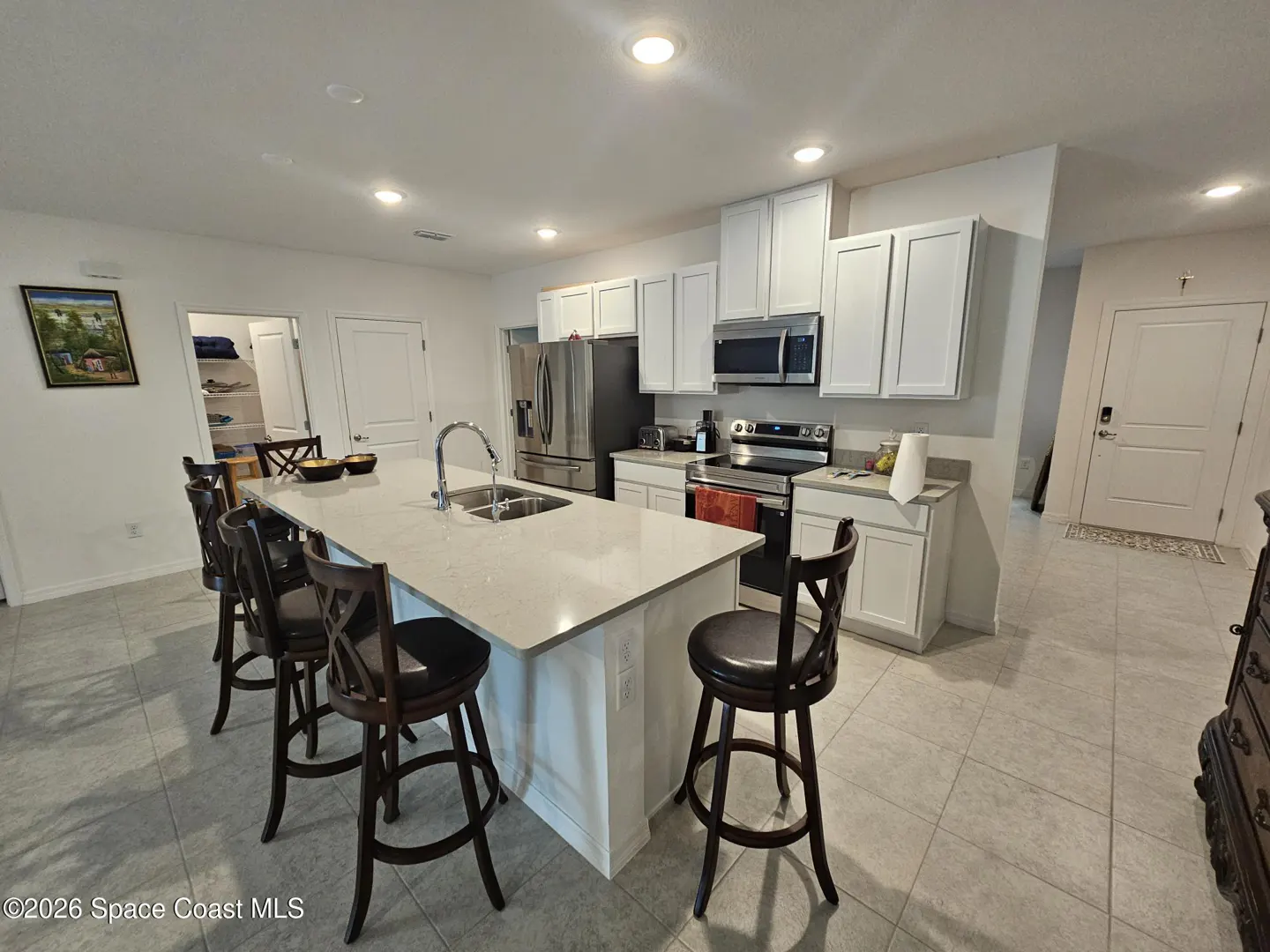 Bright, modern kitchen with white cabinets, stainless steel appliances, and a large island with dark wood stools.