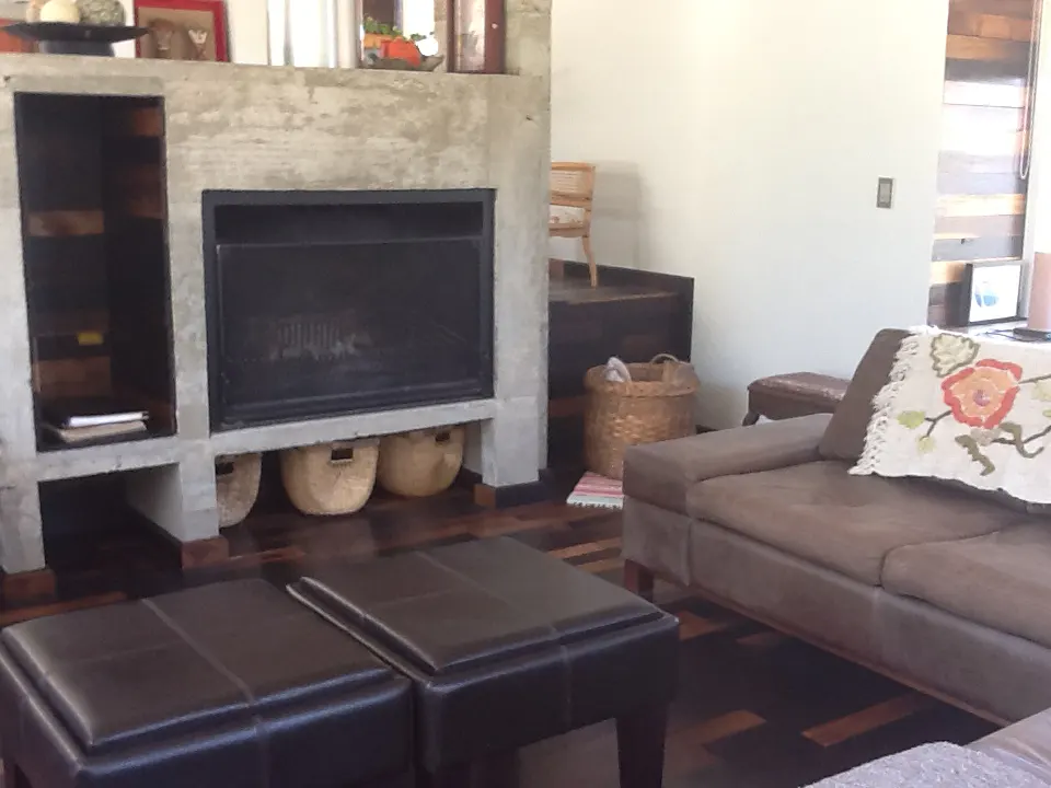 Living room with a brown sofa, two dark brown ottomans, and a concrete fireplace with three baskets underneath.