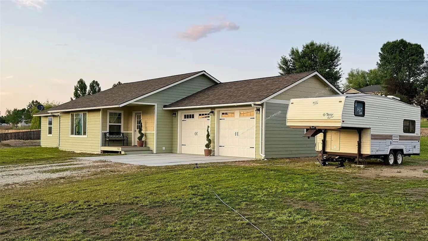 A light green house with a two-car garage and a camper parked on the lawn.