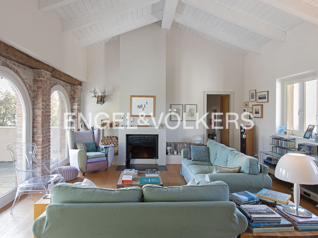 Bright living room with vaulted ceiling, exposed brick arches, and light green sofas. A fireplace and eclectic decor add warmth.