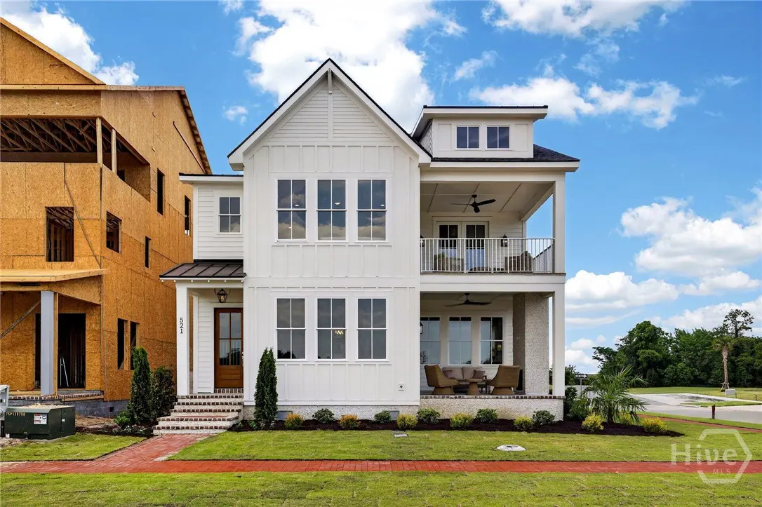 Two-story white house with a brown door, black roof, and two balconies. A red brick walkway leads to the front door. Blue sky background.