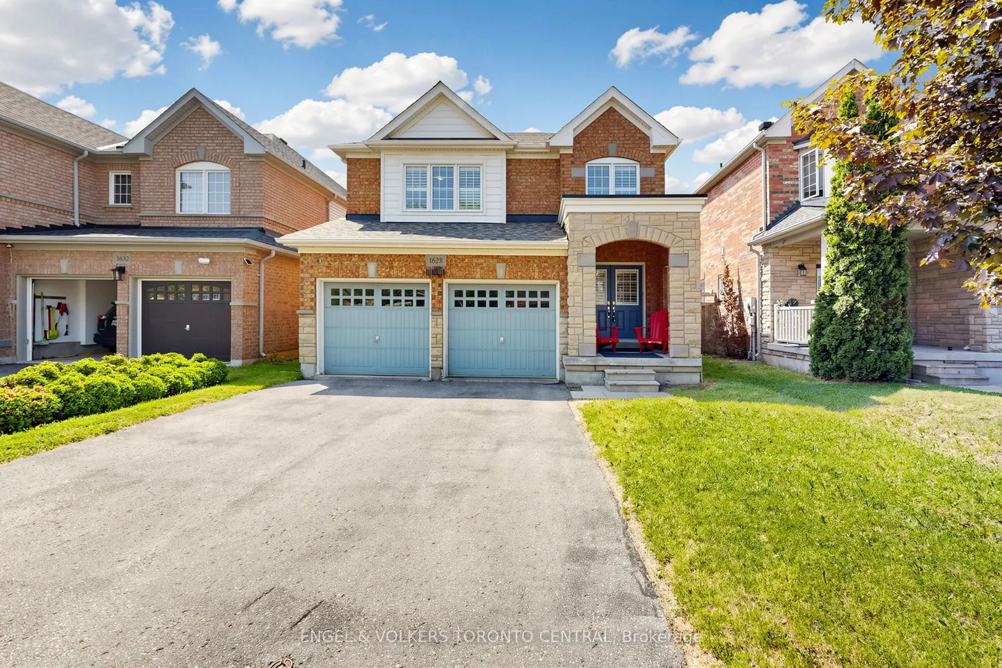 Two-story brick suburban home with a double garage, blue doors, and a paved driveway under a bright blue sky.