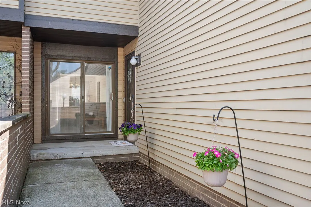 Exterior view of a home with beige siding, a sliding glass door, and hanging flower baskets.