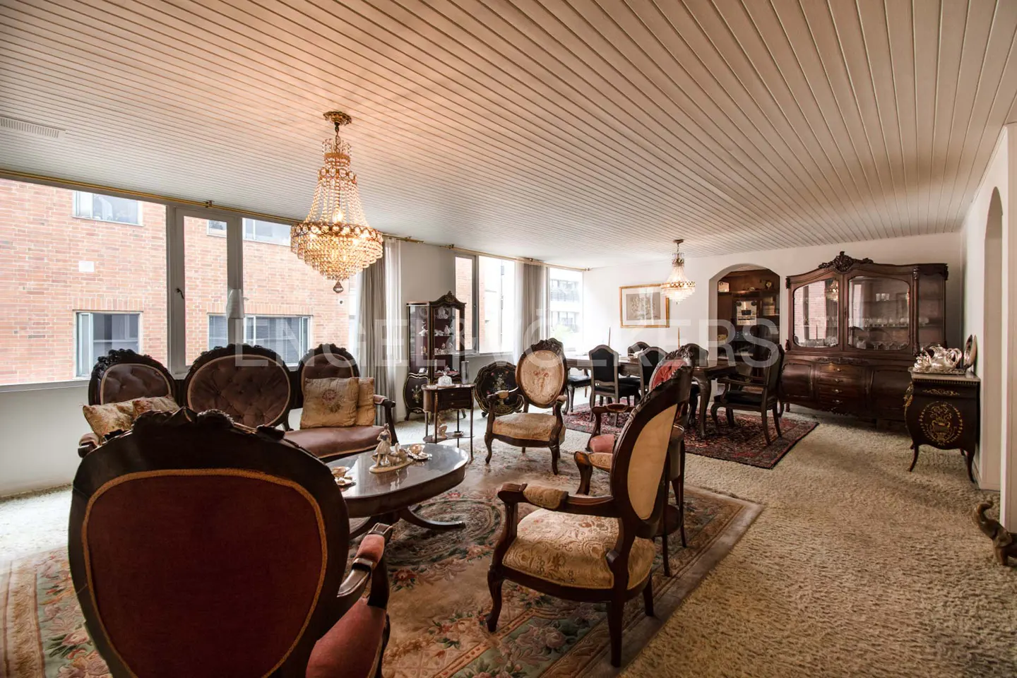 A spacious living and dining room with antique furniture, a crystal chandelier, and large windows.