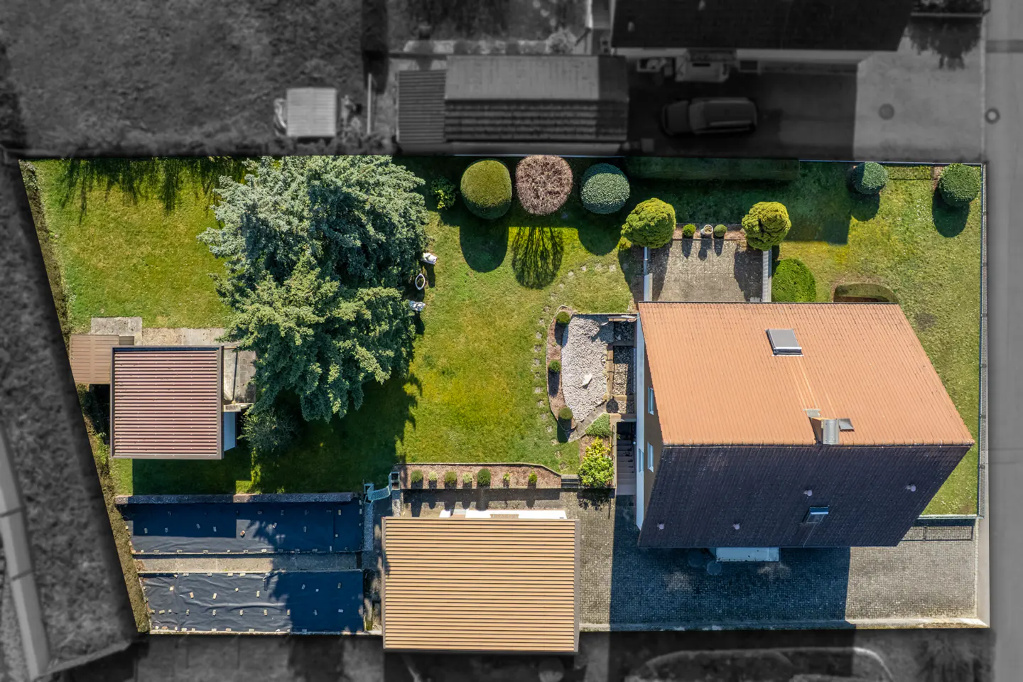 Aerial view of a house with a brown roof, green lawn, trees, and a patio. The surrounding area is desaturated.