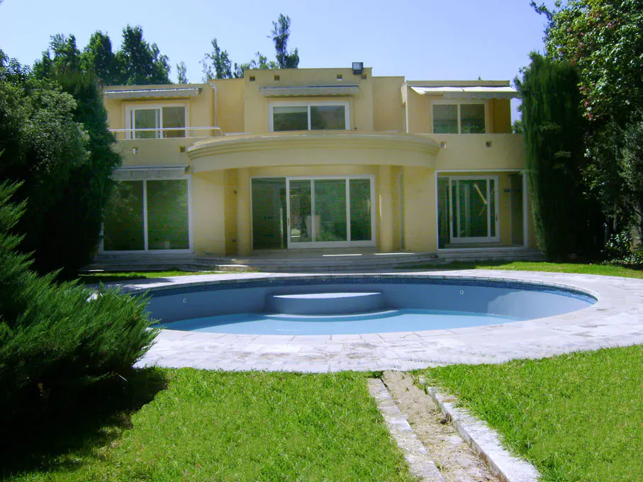 Two-story yellow house with a round swimming pool in the front yard surrounded by green grass and trees.