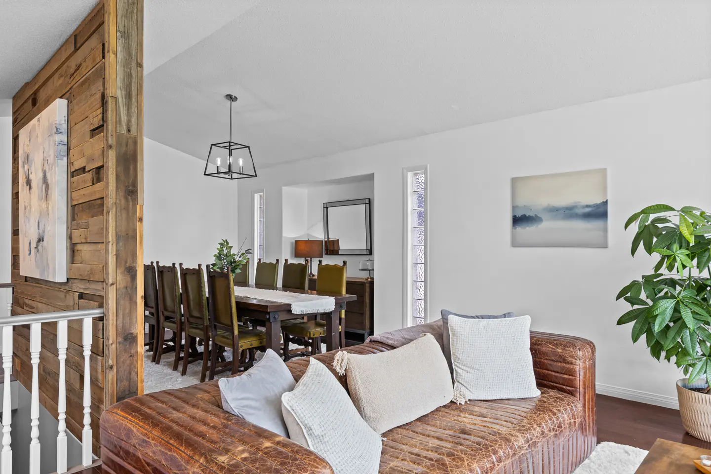 Living room with a distressed brown leather sofa, white pillows, and a dining area with a wooden table and chairs.