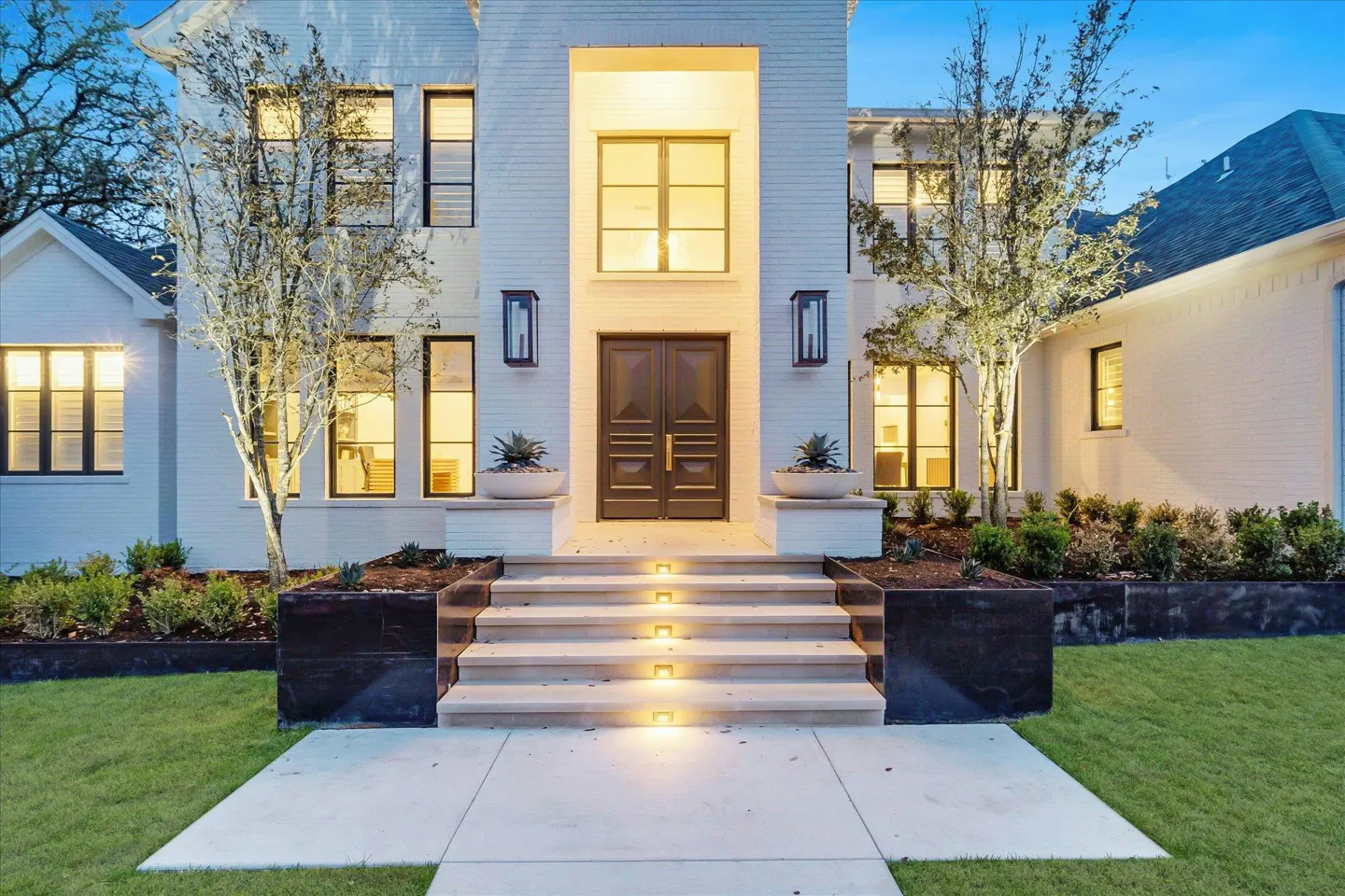 Exterior shot of a white brick house with a gray double door and illuminated steps.