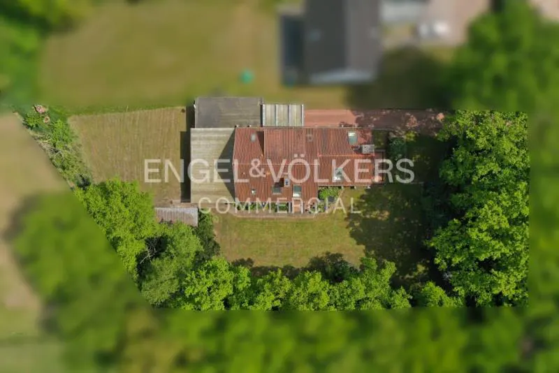 Aerial view of a commercial property with a red tile roof, surrounded by green trees and lawn. The Engel & Völkers logo is superimposed on the image.